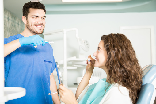 Image of a young woman being shown how to properly brush her teeth to prevent poor oral health at Irvine Dentistry.