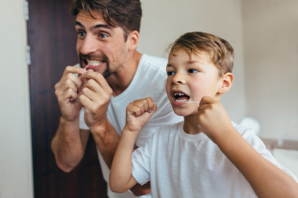 Young boy and father flossing teeth next to each other in bathroom after getting some tips from.jpg Irvine Dentistry